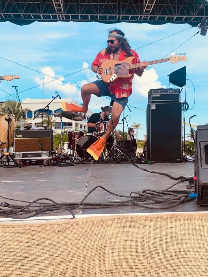 Jumping mid-air with a bass on an outdoor stage, wearing swim fins